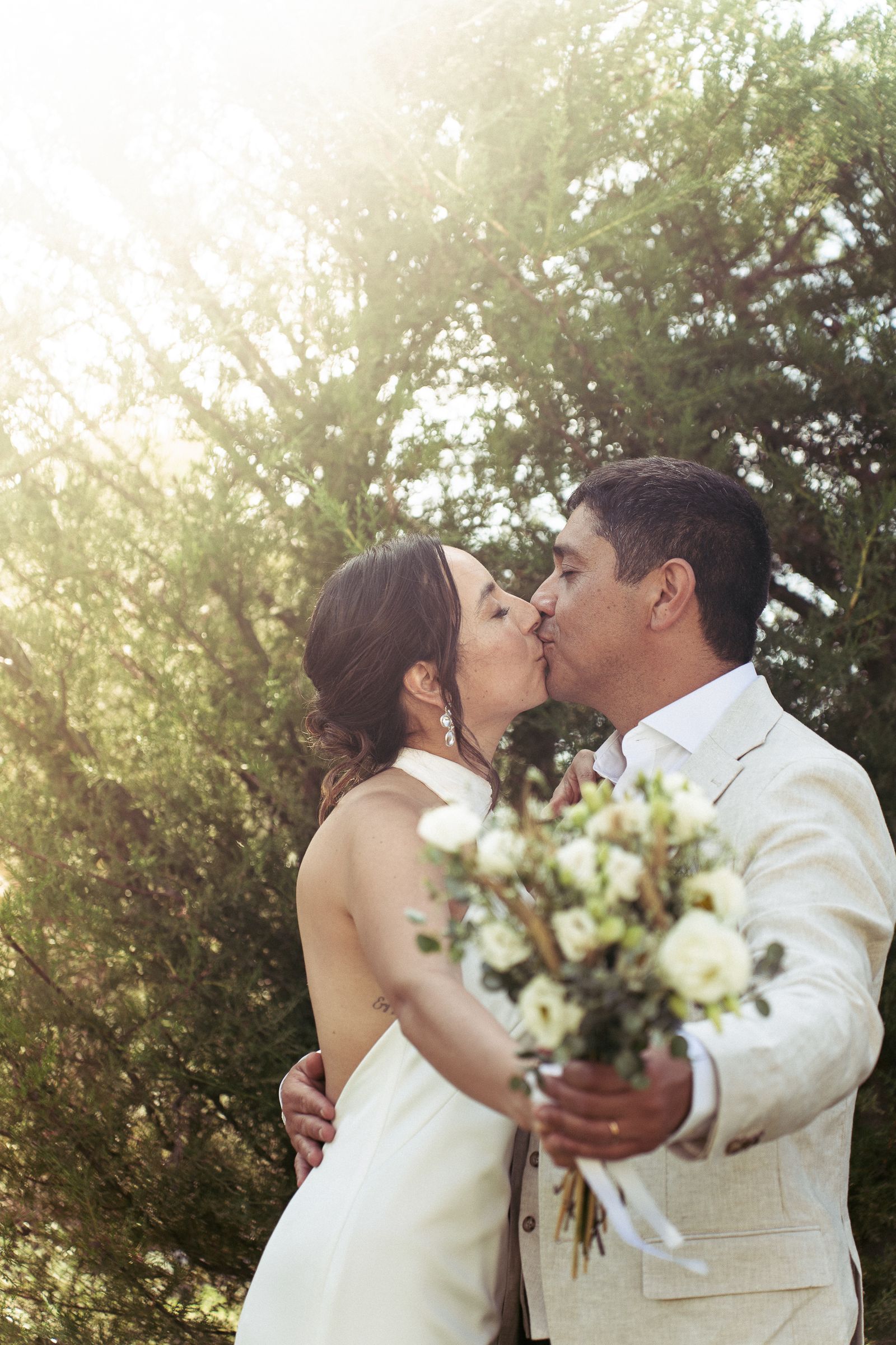Los novios besándose con el sol filtrándose entre los árboles