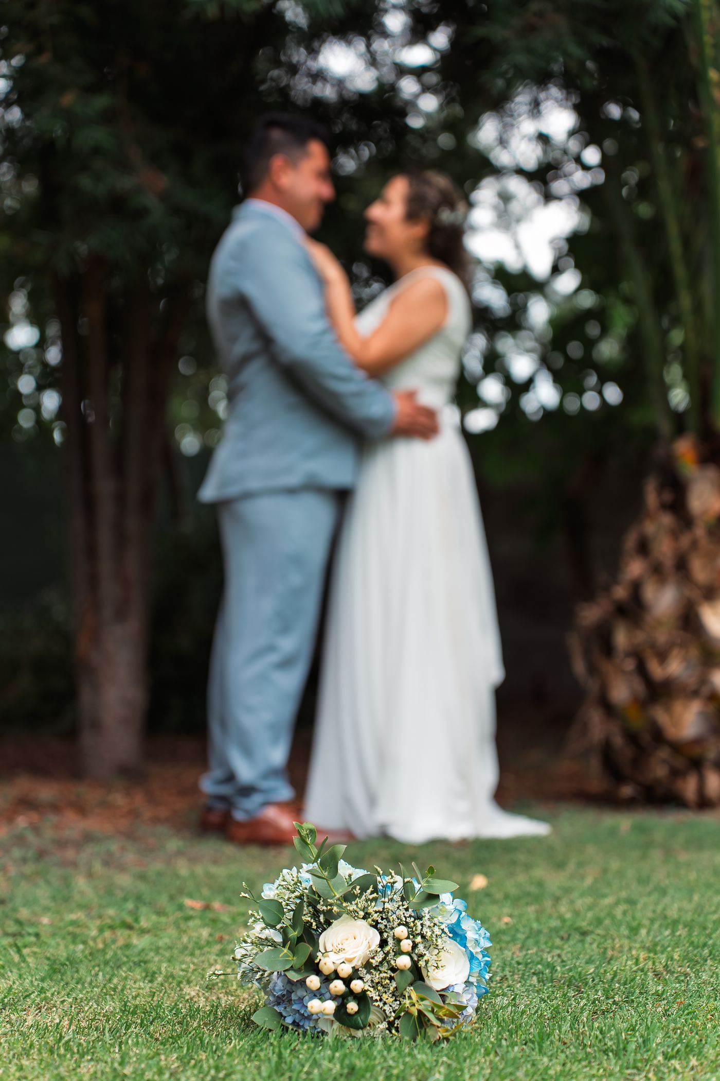 Los novios abrazados en un jardin con arboles al fondo