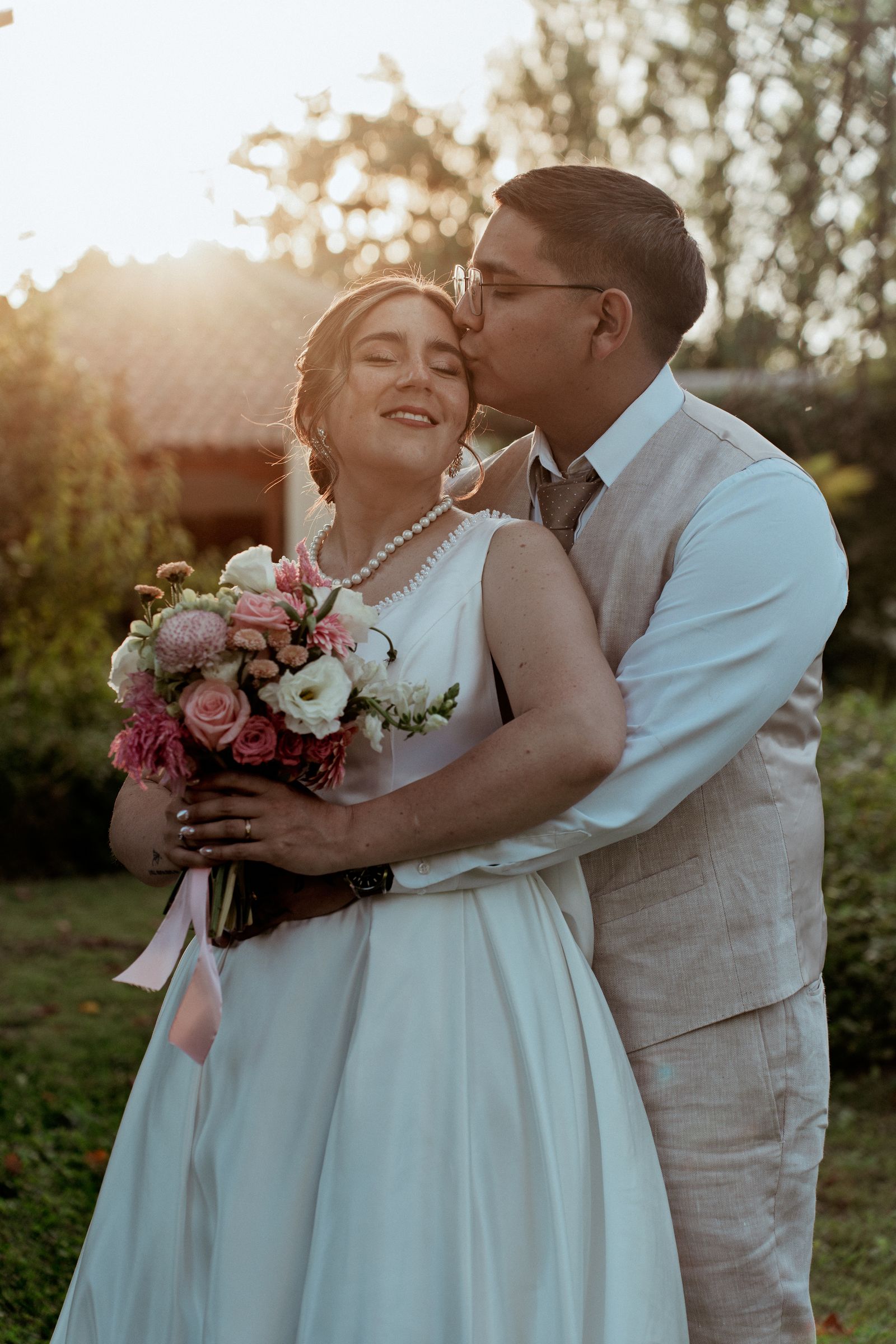 Novios abrazados con el sol del atardecer detrás, en un jardín