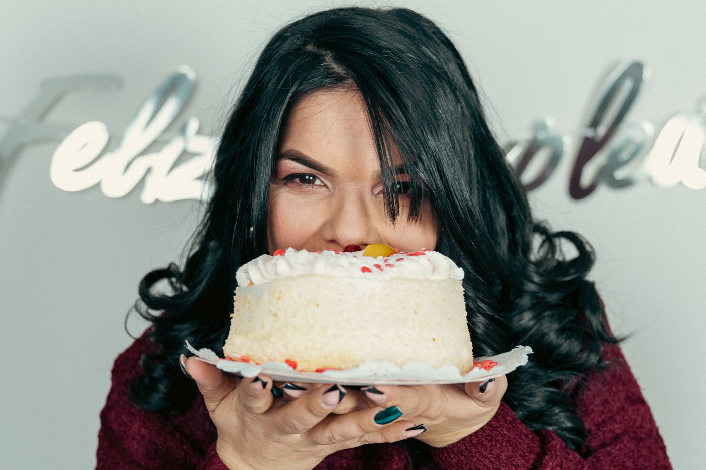 Mujer sosteniendo una torta de cumpleaños frente a su rostro entre globos
