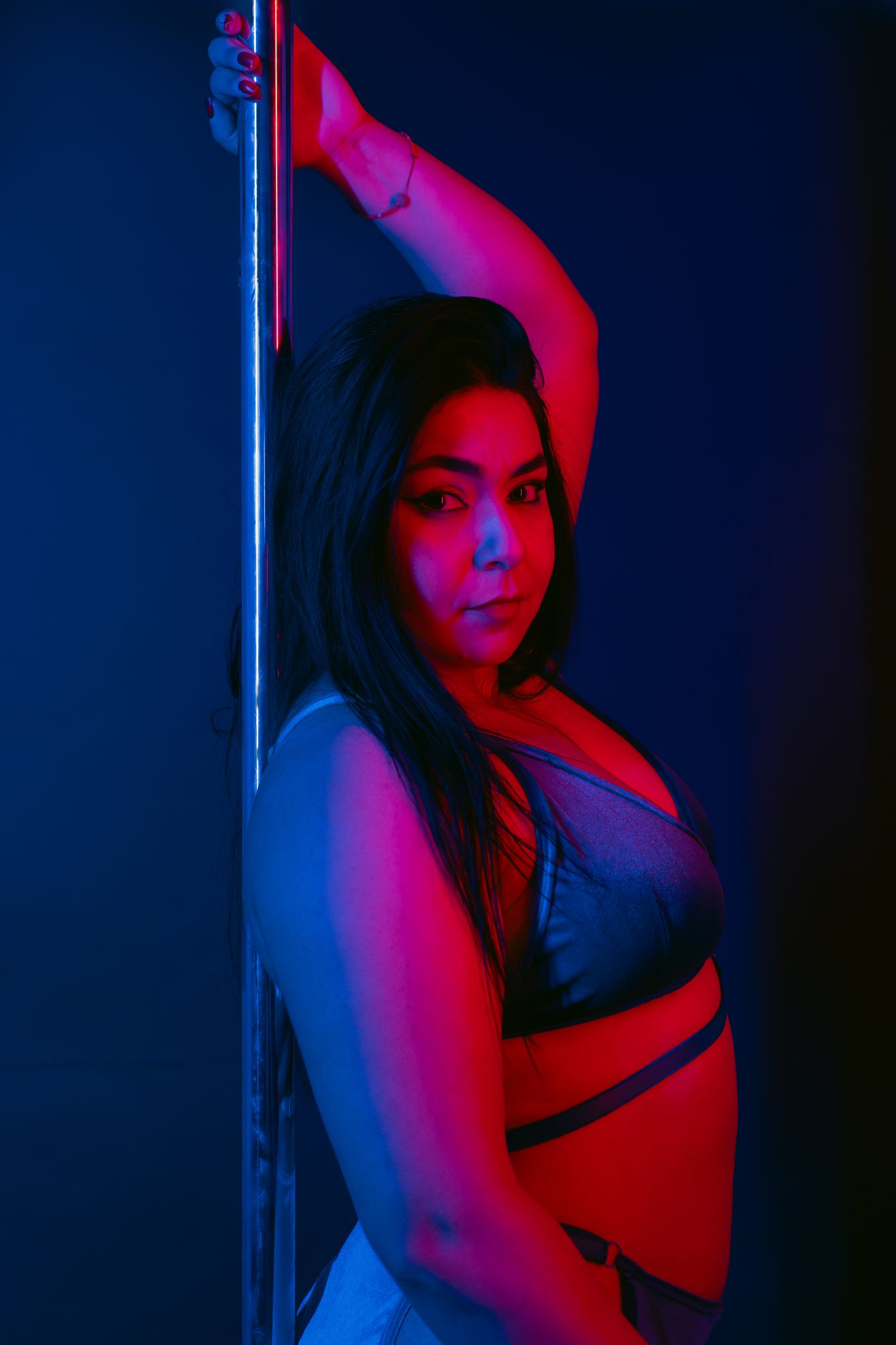 Bailarina de pole dance iluminada con luces de gel azules y rojas