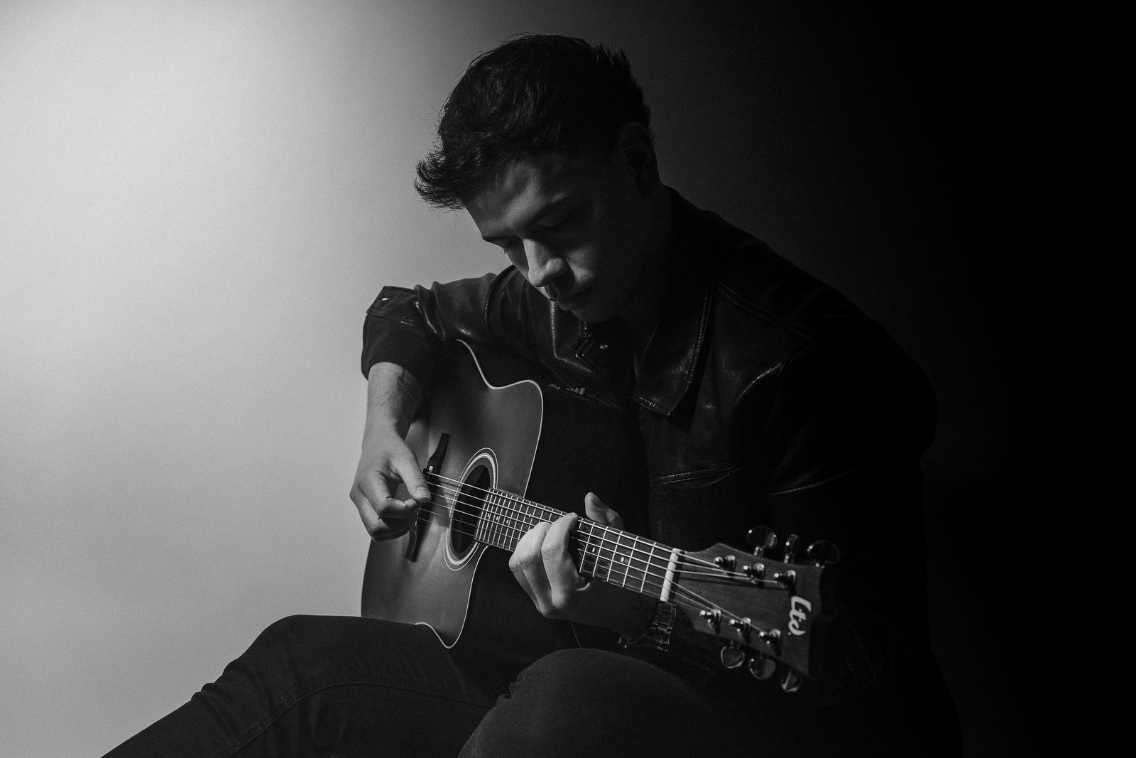 Retrato de estudio de un músico con guitarra, iluminado con luz lateral sobre fondo oscuro
