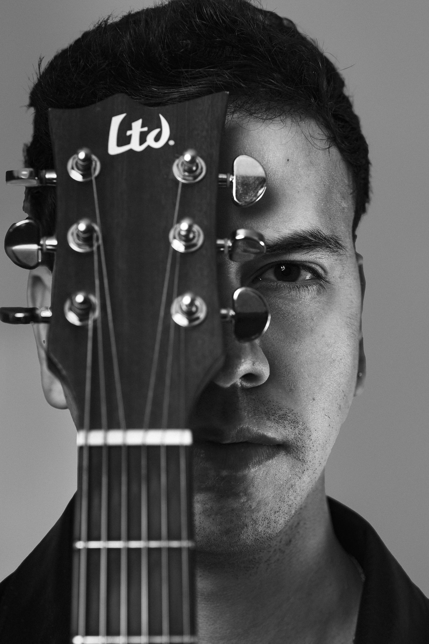 Retrato de estudio de un músico con el clavijero de la guitarra cubriendo medio rostro